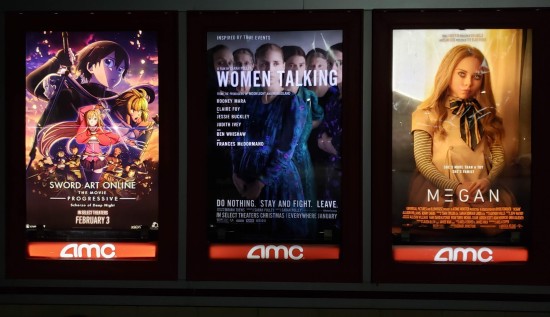 The "Women Talking" movie poster hanging outside a theater at night next to two other posters for female-led films.