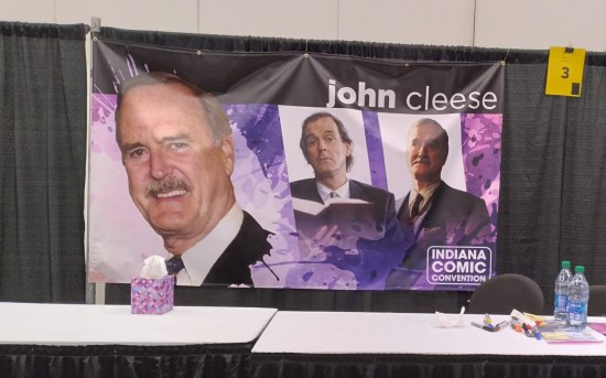 Autograph table with a John Cleese banner hanging behind it. Photos of him come from Monty Python, "A Fish Called Wanda", and something more recent, possibly even dignified, or perhaps not.