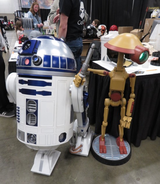 Life-sized R2D2 and Pit Droid statues in front of a booth selling helmets created using #-D printers.