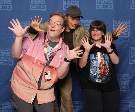Us doing jazz hands with Mads Mikkelsen! He wears a gray cap. I crouched down to Anne's height, so he leaned down to meet us there.